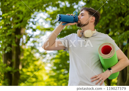 Athletic fitness sport runner man with yoga mat drinking water from bottle after training exercise 119027379