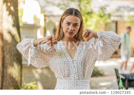Displeased woman showing thumbs down sign gesture disapproval dissatisfied bad work on city street Displeased woman showing thumbs down sign gesture disapproval dissatisfied bad work on city street 119027385