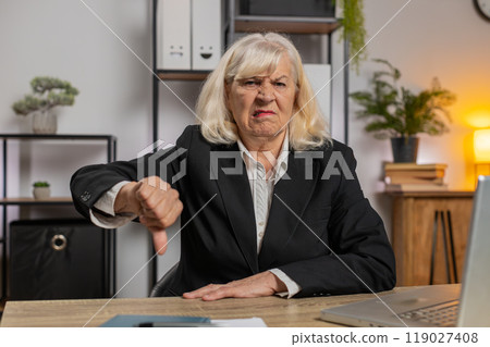 Upset senior businesswoman girl showing thumb down gesture expressing bad work at home office table Upset senior businesswoman girl showing thumb down gesture expressing bad work at home office table 119027408