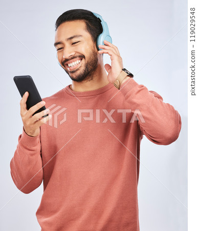 Man, smile and smartphone with headphones, listening to music or podcast isolated on studio background. Male person is enjoying radio streaming, online with wireless technology and playlist on app 119029548