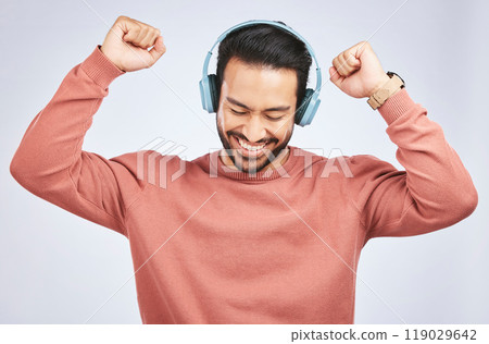 Man, headphones and dance to music in studio, white background and celebrate with energy. Happy, excited and young asian male model listening to audio, streaming sound and hearing rave song on radio 119029642