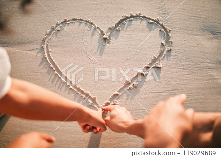 Hands, drawing and heart on beach sand for care and couple with kindness or support together with emoji. Draw, love or writing symbol in the shape of loving, caring or line in the for romance Hands, drawing and heart on beach sand for care and couple with kindness or support together with emoji. Draw, love or writing symbol in the shape of loving, caring or line in the for romance 119029689
