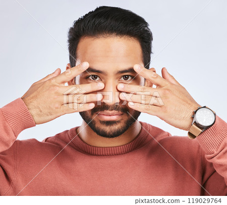 Portrait, eyes and asian man with fingers on face in studio with confidence, personality and persona on grey background. Hands, pose and male person with hand gesture for mask, masquerade or ego 119029764