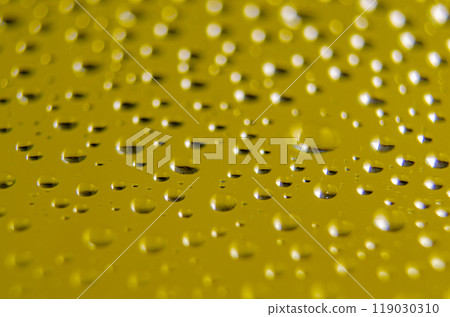 Side view of raindrops forming patterns on a smooth surface on yellow background. Fresh rain texture 119030310