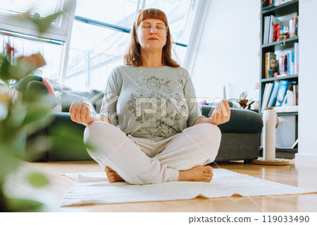 portrait of middle aged woman meditating, yoga at home 119033490