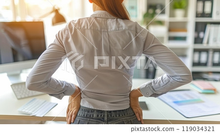 Woman holding her back in pain, experiencing discomfort after prolonged sitting at work. 119034321