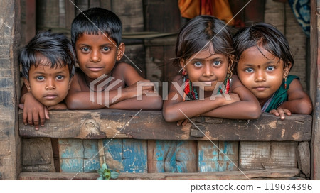 Four curious children with big eyes peer out from rustic window in their Indian village home. 119034396