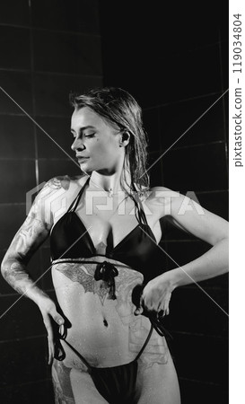 Sexy woman fashion model takes a shower in a swimsuit, posing for the camera. Monochrome photography. 119034804