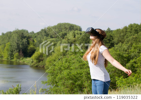 Young woman uses virtual reality glasses with her arms outstretched 119035322