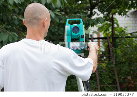 A male surveyor works with a total station device, from the back 119035377