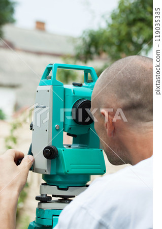 A male surveyor works with a total station device, close-up 119035385