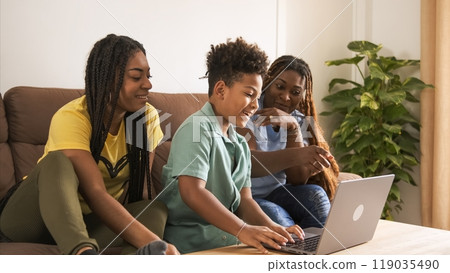 Cheerful boy using laptop with mother and sister while sitting on sofa at home Cheerful boy using laptop with mother and sister while sitting on sofa at home 119035490