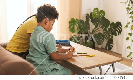 Little boy coloring in book with young sister on table at home Little boy coloring in book with young sister on table at home 119035491