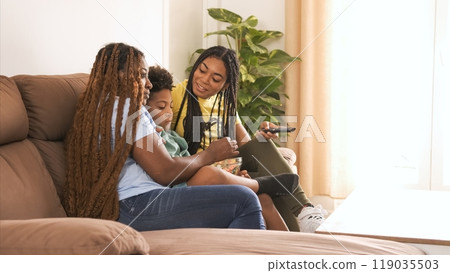 Happy woman looking at brother while using remote control with mother on sofa Happy woman looking at brother while using remote control with mother on sofa 119035503