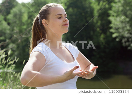 Healthy, calm, young woman meditating in nature, doing breathing exercises, relaxing body and mind. Mental health and stress-free meditation. 119035524