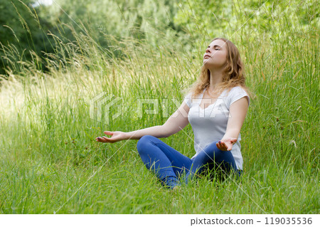 Woman meditating in nature with eyes closed, doing breathing exercises, relaxing body and mind. Mental health and stress-free meditation. Woman meditating in nature with eyes closed, doing breathing exercises, relaxing body and mind. Mental health and stress-free meditation. 119035536