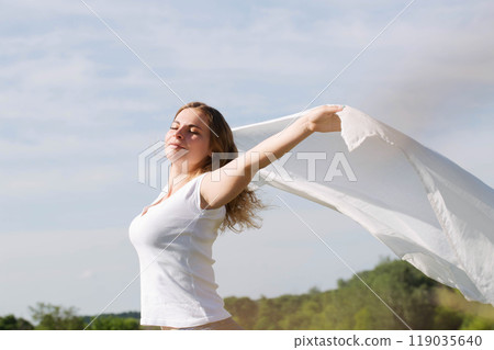A young woman holds a white cloth in her hands, the concept of purity and freedom A young woman holds a white cloth in her hands, the concept of purity and freedom 119035640