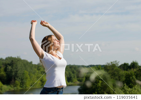A beautiful young woman rests in nature with her arms outstretched A beautiful young woman rests in nature with her arms outstretched 119035641