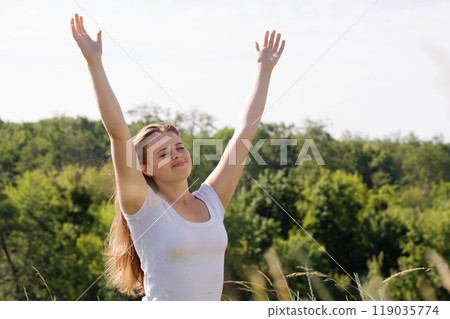 A beautiful young woman rests in nature with her arms outstretched A beautiful young woman rests in nature with her arms outstretched 119035774