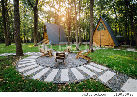 Modern wooden A-frame cabins in forest with outdoor seating and fire pit area, relaxation time Modern wooden A-frame cabins in forest with outdoor seating and fire pit area, relaxation time 119036085