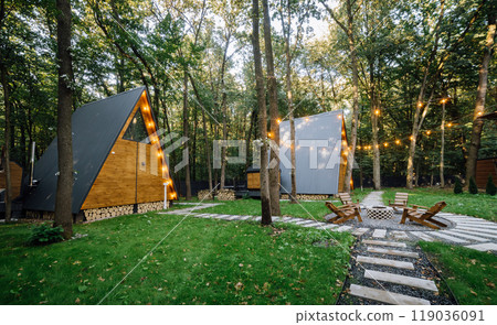 Modern wooden A-frame cabins in forest with outdoor seating and fire pit area, relaxation time Modern wooden A-frame cabins in forest with outdoor seating and fire pit area, relaxation time 119036091