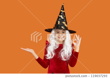 Girl witch in Halloween costume isolated on orange. All Hallows holiday sale. All Hallows advertisement. October 31. Girl in witch costume. Presenting product. Happy Halloween. Ok Girl witch in Halloween costume isolated on orange. All Hallows holiday sale. All Hallows advertisement. October 31. Girl in witch costume. Presenting product. Happy Halloween. Ok 119037293
