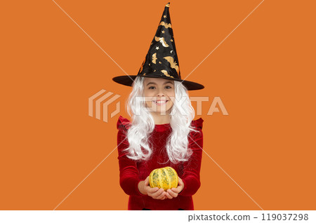 Halloween pumpkin in hand of witch girl. Halloween witch girl isolated on orange. Pumpkin on Halloween. Witch All Hallows costume of girl. October 31 pumpkin. Costume party. Enchanted pumpkin Halloween pumpkin in hand of witch girl. Halloween witch girl isolated on orange. Pumpkin on Halloween. Witch All Hallows costume of girl. October 31 pumpkin. Costume party. Enchanted pumpkin 119037298