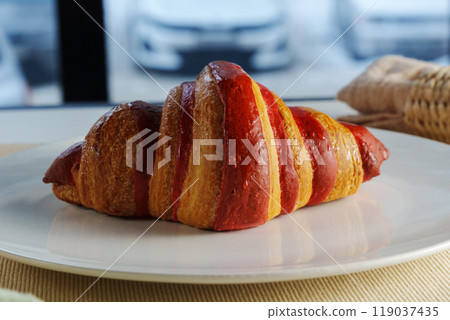 A freshly baked croissant, perfectly golden and flaky, rests on a plate next to a soft linen napkin, creating a warm atmosphere. A freshly baked croissant, perfectly golden and flaky, rests on a plate next to a soft linen napkin, creating a warm atmosphere. 119037435