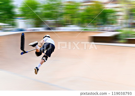 Young man practicing Scootering (Freestyle Scootering) in the new SkatePark in the central park of Igualada, Barcelona, Spain. blurred background 119038793