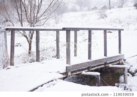wooden bridge covered with snow over a stream 119039059