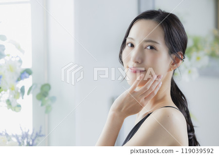A woman in a black camisole dress standing by the window 119039592