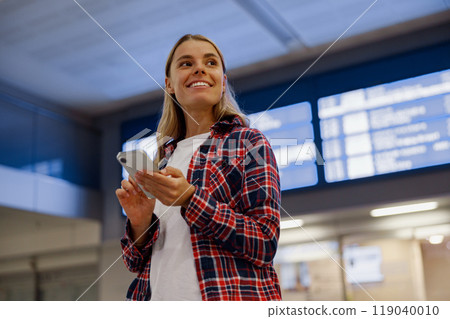 A smiling young woman at the airport holding her phone, experiencing joy and excitement 119040010