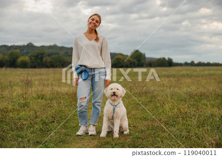 A woman enjoying a peaceful walk with her dog in a beautiful scenic field, surrounded by nature A woman enjoying a peaceful walk with her dog in a beautiful scenic field, surrounded by nature 119040011