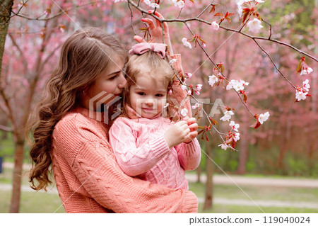 mother and little girl , hugging in the park with blooming pink sakura. mother and little girl , hugging in the park with blooming pink sakura. 119040024