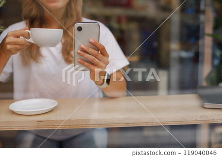 Person Enjoying Coffee while Using Smartphone in Caf Person Enjoying Coffee while Using Smartphone in Caf 119040046