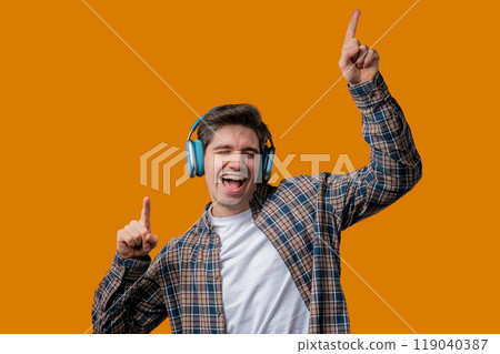 Young positive man listening music, enjoying with headphones, yellow studio Young positive man listening music, enjoying with headphones, yellow studio 119040387