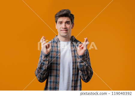 Adult 30s man praying with crossed fingers on yellow background. Guy begs God help Adult 30s man praying with crossed fingers on yellow background. Guy begs God help 119040392
