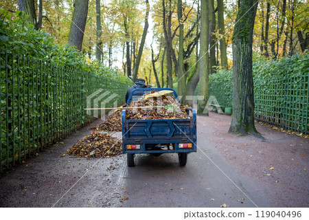 Janitor on small dump truck cleaning leaves in autumn park riding asphalt road. Janitor on small dump truck cleaning leaves in autumn park riding asphalt road. 119040496