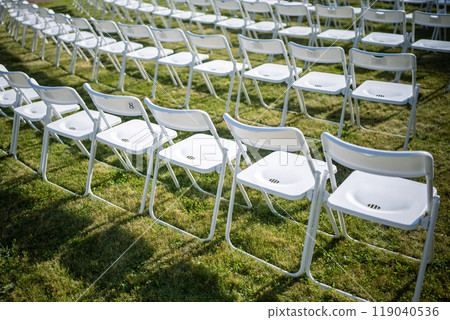 Folding chairs standing in row on green grass, casting shadow on ground. Outdoor party preparation Folding chairs standing in row on green grass, casting shadow on ground. Outdoor party preparation 119040536