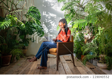 Smiling African american woman with laptop. Black girl using portable computer sitting among garden 119040552