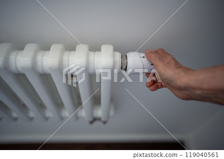 Woman hand adjusting radiator thermostat, testing temperature. Chilly indoor, economy and inflations 119040561