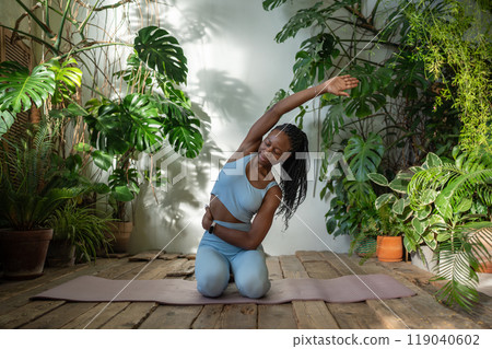 Healthy body with fitness. Active african american woman stretching hand aside sitting on sports mat 119040602