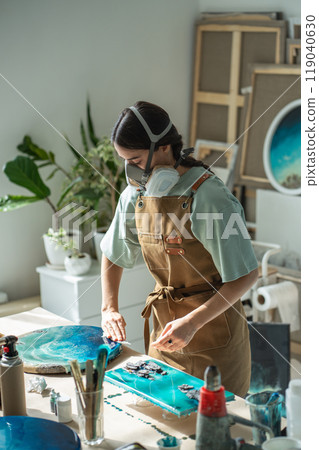 Female artist creating epoxy resin paintings on workbench equipped for professional creative work. 119040630