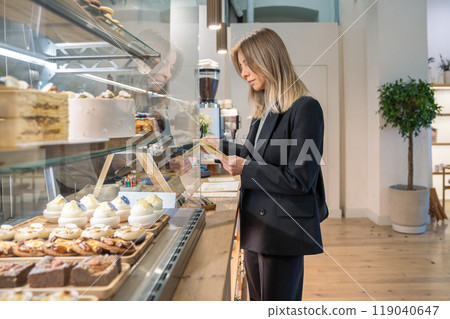 Focused coffee shop female owner inspecting establishment before opening, attentively checking menu. 119040647