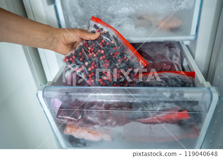 Girl hand taking frozen lingonberry, blueberry mix in bag from freezer. Stocking up for winter, diet 119040648
