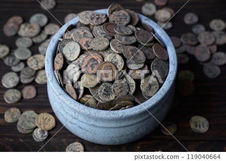 Roman coin hoard on dark wooden table, lot of Ancient money in old ceramic pot, vintage background. Concept of pile, antique, Empire, civilization and history. Roman coin hoard on dark wooden table, lot of Ancient money in old ceramic pot, vintage background. Concept of pile, antique, Empire, civilization and history. 119040664