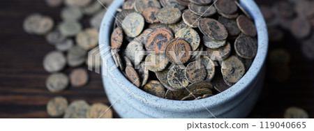 Roman coin hoard on dark wooden table, Ancient money in old ceramic pot, wide banner for vintage background. Concept of pile, antique, texture, civilization Roman coin hoard on dark wooden table, Ancient money in old ceramic pot, wide banner for vintage background. Concept of pile, antique, texture, civilization 119040665