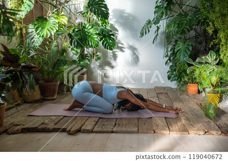 Black sportswoman lying on fitness mat do stretching exercise relaxing back muscles in urban jungle. Black sportswoman lying on fitness mat do stretching exercise relaxing back muscles in urban jungle. 119040672