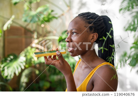 Interested african american young woman records voice message using smartphone speaking latest news. Interested african american young woman records voice message using smartphone speaking latest news. 119040676