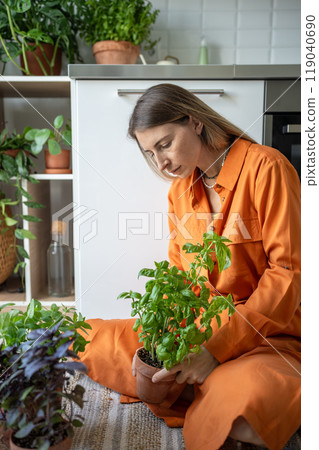 Interested woman tends home seedlings herbs by sit on floor focusing on interacting with houseplants 119040690